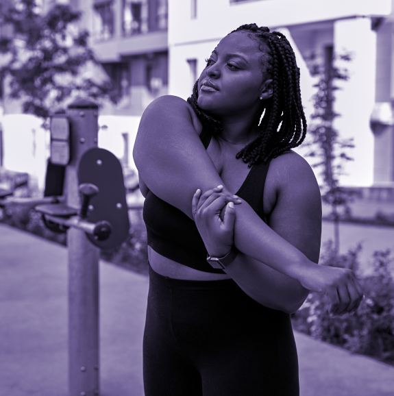 Black and white photo of young woman in exercise gear stretching her arm in a city landscape